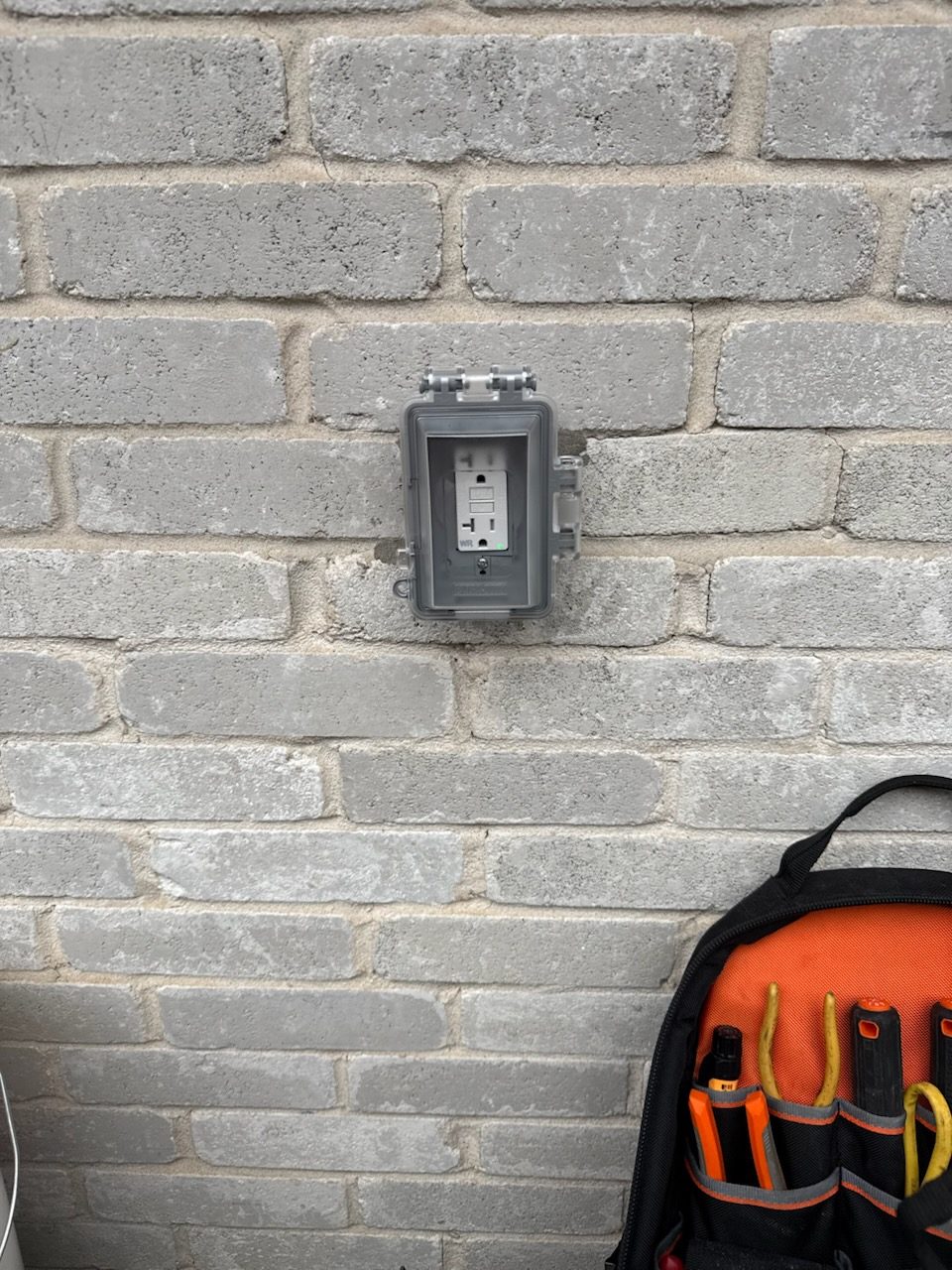 Updated outdoor receptacle with a gray weatherproof outlet cover mounted on a brick wall